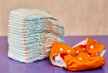 A large pile of disposable nappies next to a single reusable nappy 