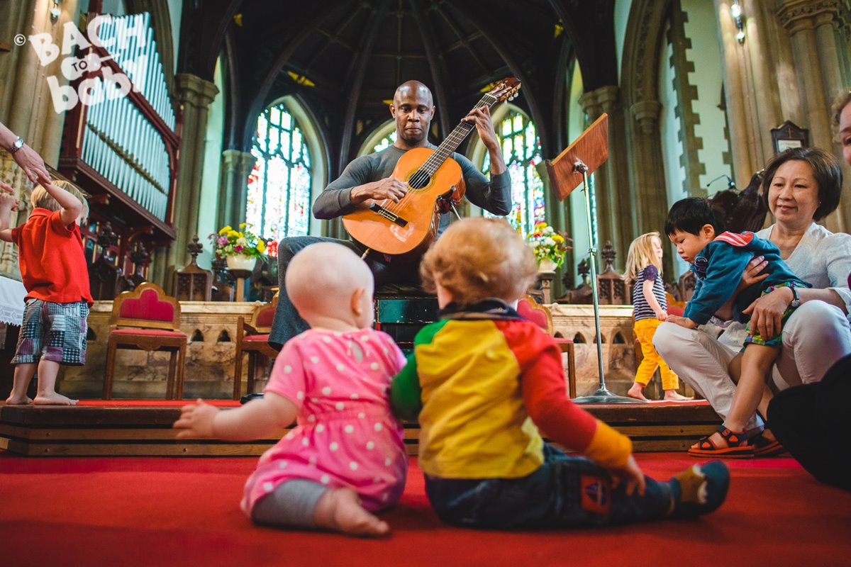 article thumb - Ahmed Dickinson, one of our friendly musicians, playing guitar to some tots and families