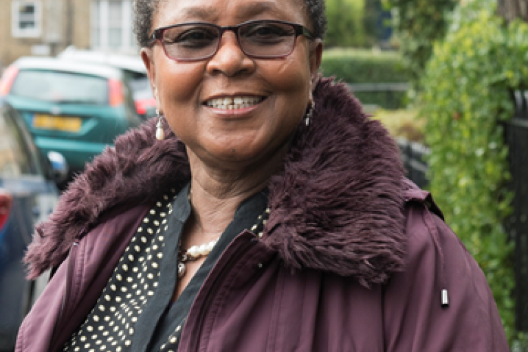 Picture of black woman standing on a residential street, smiling at the camera.