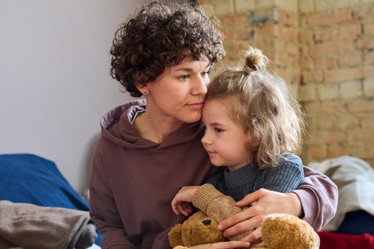 Woman with a concerned expression cuddling little girl.