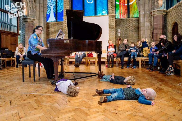 toddlers lie on the floor next to a bach to baby pianist