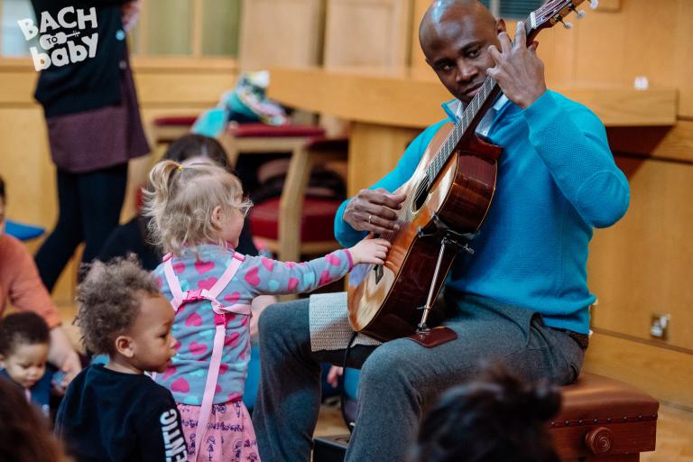 child investigates bach to baby guitarist
