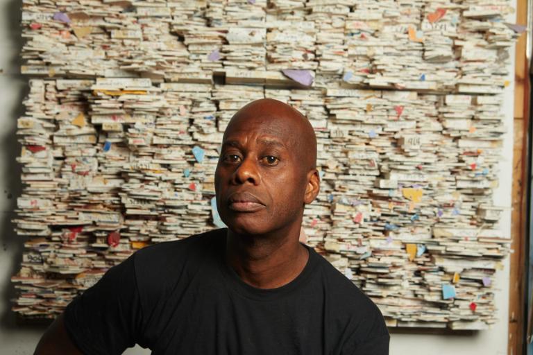 Artist Leonardo Drew sits in front of one of his works of art. 