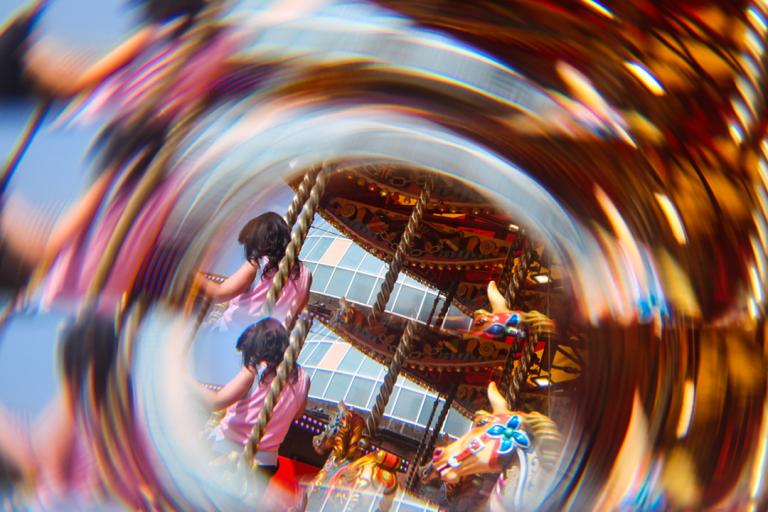 A blurry, kaleidoscopic  style photo of a figure wearing pink on a fairground carousel 
