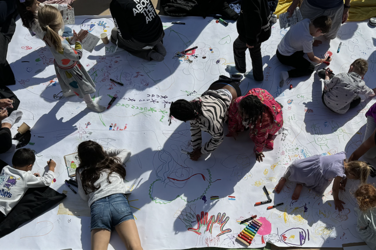 Birdseye view of children drawing on a large piece of paper on the floor