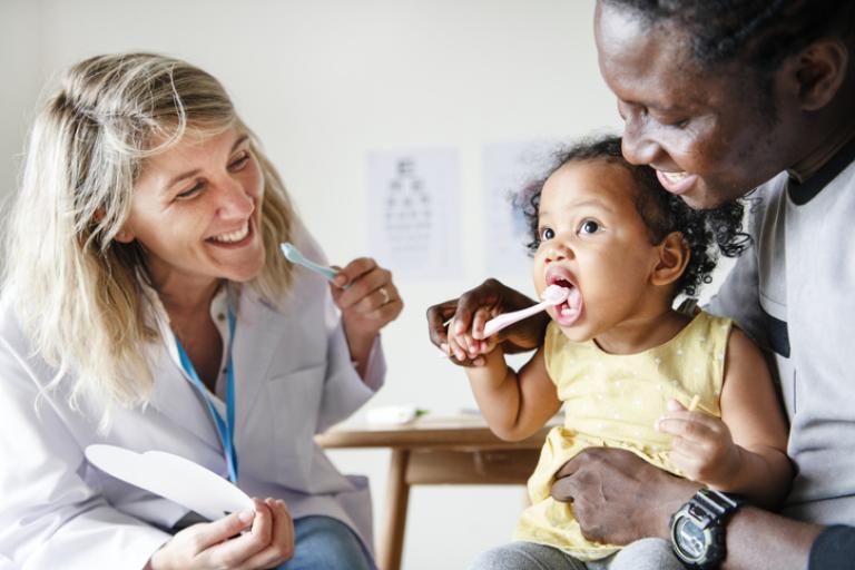 Health visitor showing a young child how to clean her teeth