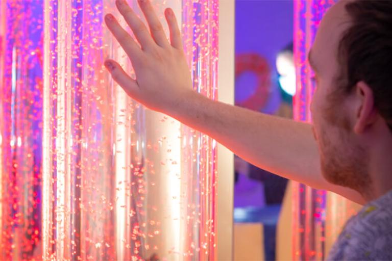 A man reaching out to touch a glowing pillar in a multisensory room