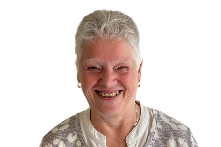 A woman with short grey hair wearing a grey and white patterned top and a silver necklace