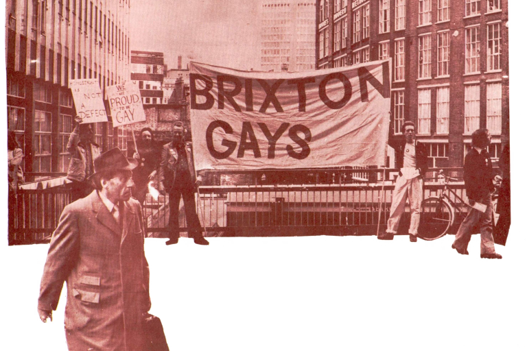 Protesters hold a large "Brixton Gays" banner and signs reading "We are proud to be gay" and "Homosexuality is not a defect" on a city street, while a man in a coat walks past.