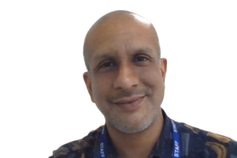 A man with cropped grey hair and a beard, wearing a dark blue shirt
