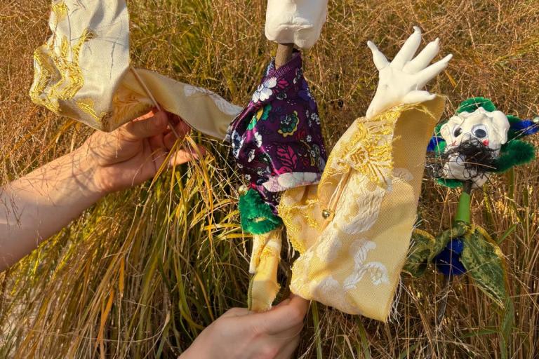 A fun monster puppet being held by two hands in front of some long grass