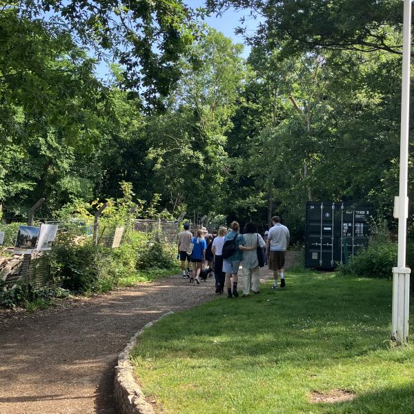 A group walk through the luscious greenery of Nunhead Cemetery. The sky is blue with grass in the foreground.