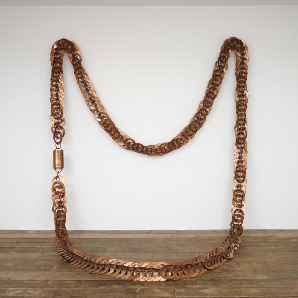 A large sculpture hanging in an art gallery. The sculpture is a giant copper necklace.