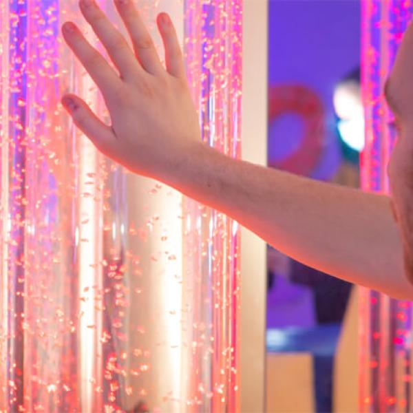 A man reaching out to touch a glowing pillar in a multisensory room