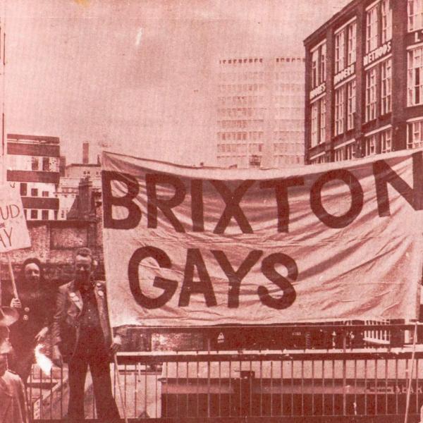 A sepia tone image of a protest march from the 1970s, with two men holding up a large banner that reads 'Brixton Gays'