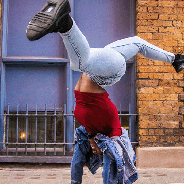 Hip-hop dancer does trick in street in summer clothes.