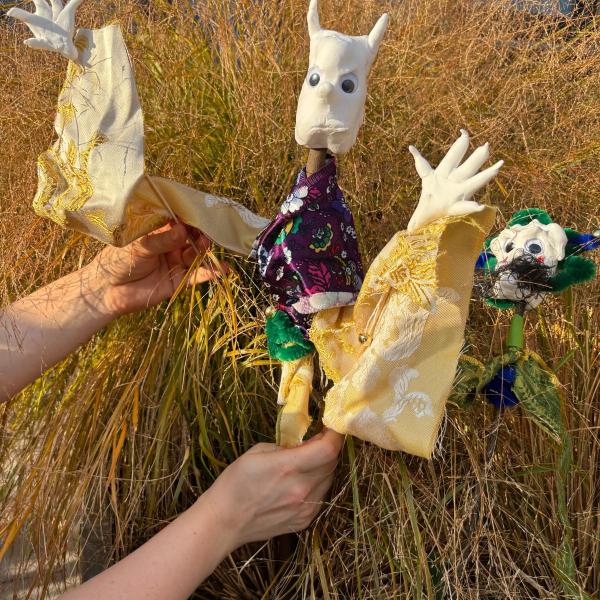 A fun monster puppet being held by two hands in front of some long grass