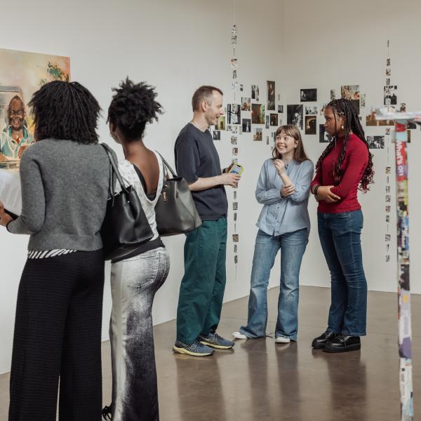 People stand around an art gallery looking at artworks and chatting. 